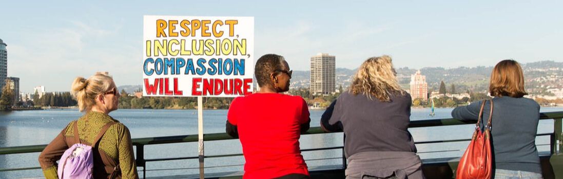 At Lake Merritt, people stand with a sign: RESPECT, INCLUSION, COMPASSION WILL ENDURE!
