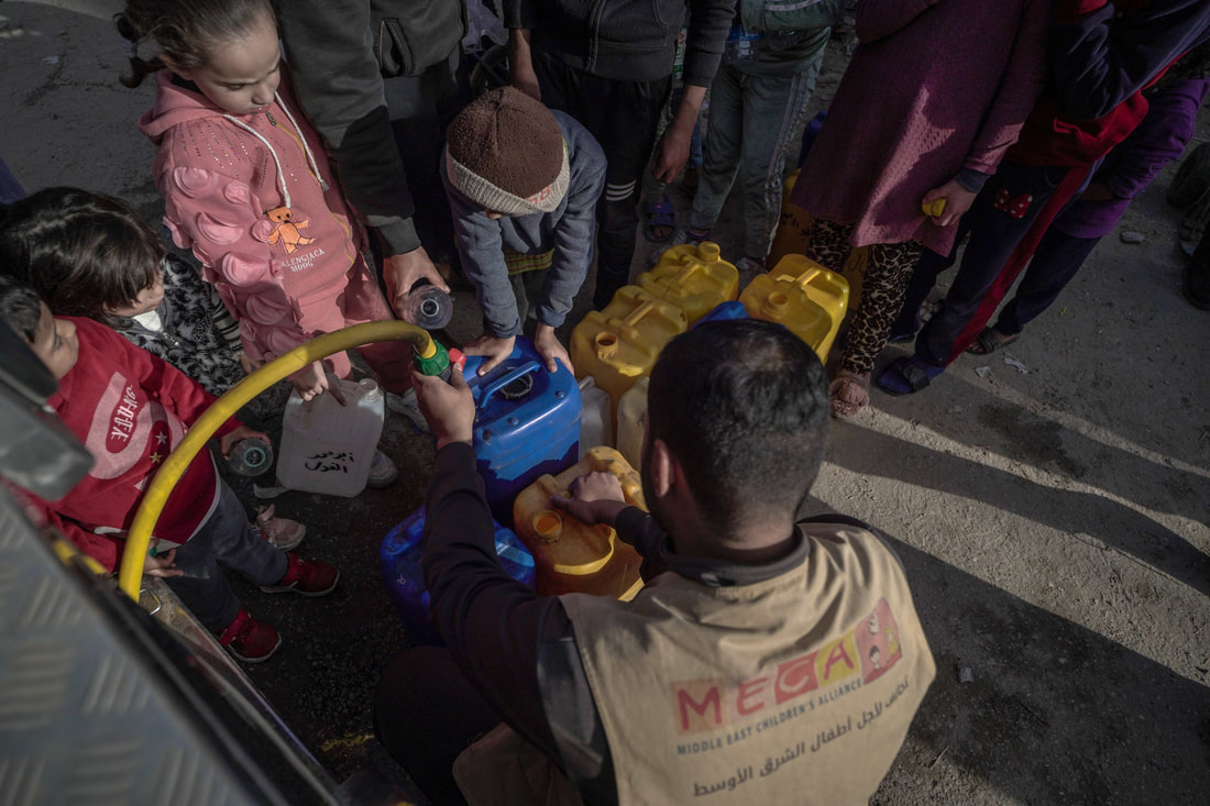 Displaced families obtain drinking water from MECA in Rafah, Gaza.  Four children hold jugs for a MECA staff to fill with drinking water, while several adults wait in line in the background. Picture