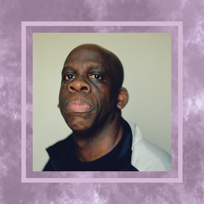 A portrait of Leroy Moore from the shoulders up. He is wearing a black t-shirt and a black and white athletic jacket. He is looking directly into the camera with a determined, unsmiling gaze. The photo is framed on a textured purple background.