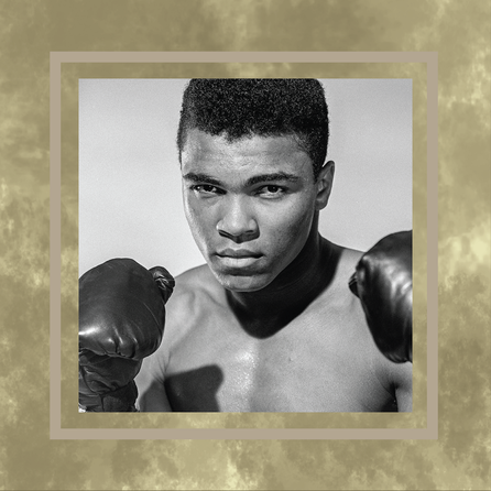  A young Muhammad Ali is seen in black and white, facing the camera, shirtless and wearing boxing gloves, squared off in a boxing stance. His picture is in a gold textured frame.
